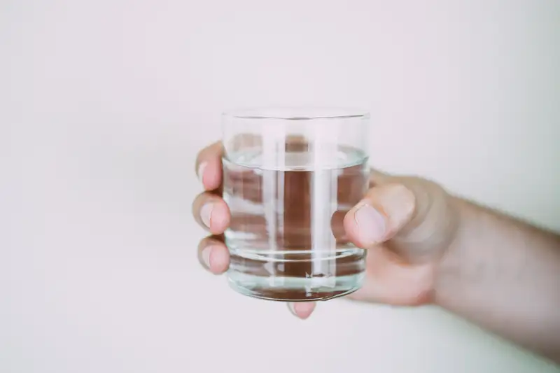 Một ly nước lọc đặt cạnh giường ngủ, ánh sáng mặt trời chiếu vào.